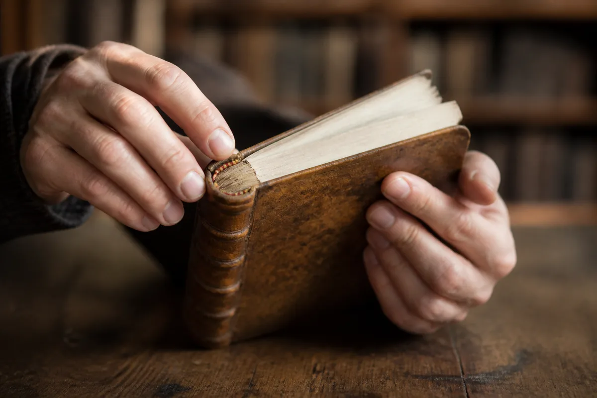 Mains d’un lecteur examinant la reliure d’un ouvrage ancien posé sur une table en bois